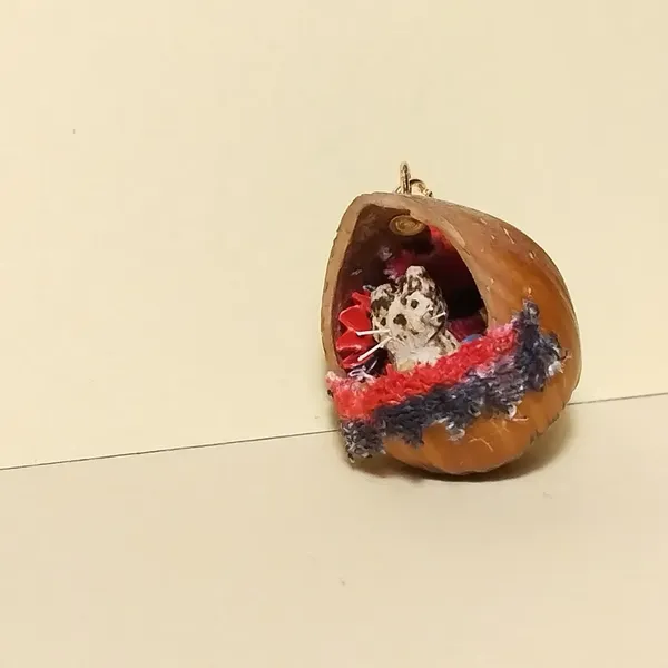 Pendentif noisette avec un chat dedans. Derrière le chat, il y a un éventail rouge. Sur le rebord, une bande de tissu rouge et noir 