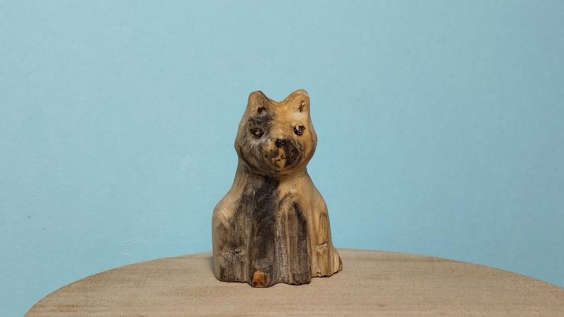 Une sculpture de chat en bois. La moitié du corps est plus foncée