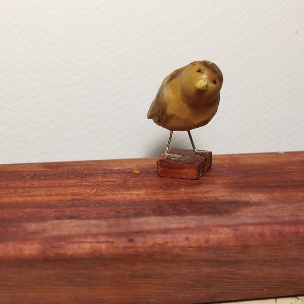 Un oiseau en bois, pattes en métal. Il penche légèrement sa tête