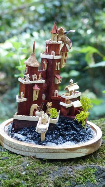 Un château miniature en bois rouge, peuplé de nombreux animaux en bois
