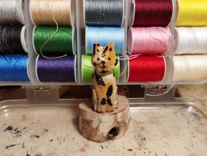 Une sculpture de chat tricolore devant des bobines de fil à coudre 