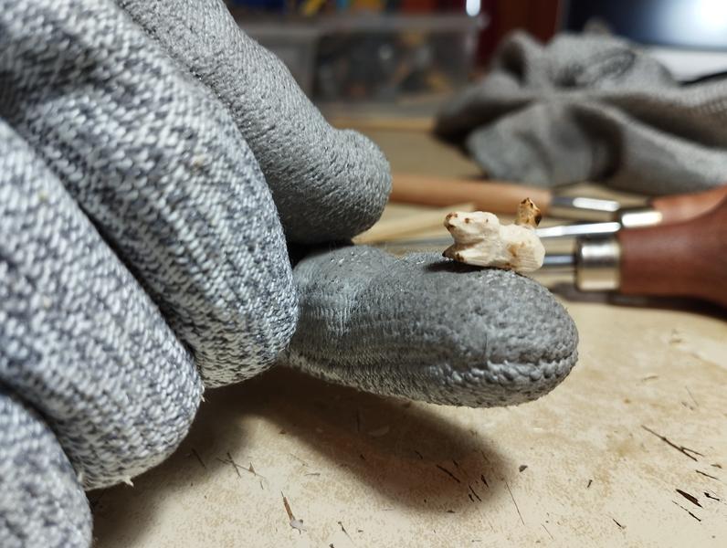 A tiny wood sculpture of capybara chilling on top of a finger (covered by gray gloves). A tiny bird sit on the capybara's back